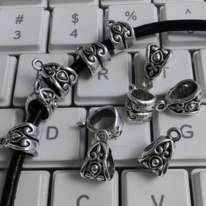 May include: A close-up of silver metal jewellery findings with ornate designs. The findings are arranged on a keyboard with black leather cord.