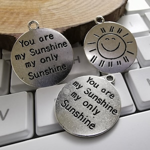 Puede incluir: Tres colgantes de plata con el texto "You are my Sunshine my only Sunshine" y un diseño de sol sonriente.