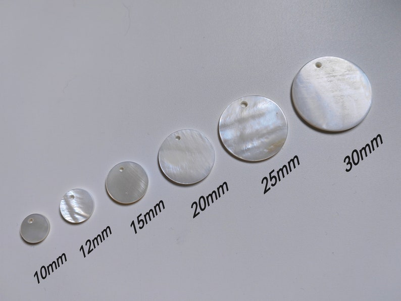 May include: Assortment of seven white mother of pearl round discs with a hole in the center. The discs range in size from 10mm to 30mm.