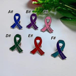 May include: Six enamel ribbon pins in shades of blue, purple, pink, green, red, and teal. Each pin has the word "Hope" and a pin back. Ideal for awareness campaigns.
