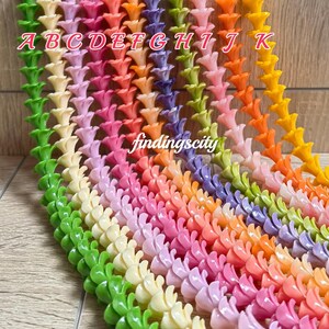 May include: Multiple strands of small, trumpet-shaped flower beads arranged in a vertical gradient of colors including green, cream, pink, orange, purple, and yellow. Each strand is labeled with letters A through K, and the text findingscity is visible.