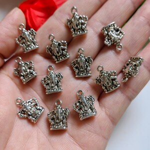 May include: A collection of small, silver-colored charms in the shape of the Hindu deity Ganesha. Each charm features intricate details and a small loop at the top for attaching to jewelry or other crafts. The charms are displayed against a neutral background.
