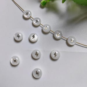 May include: White round beads with a gold lightning bolt design. The beads are strung on a gold chain.
