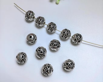 May include: A collection of silver-toned metal beads with intricate designs. The beads are round and have a hole in the center for stringing.