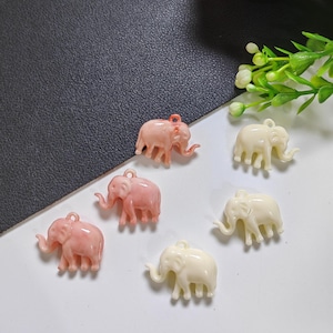 Può includere: Una collezione di piccoli ciondoli a forma di elefante nei toni del rosa e del crema. Ogni ciondolo ha un anello nella parte superiore per il fissaggio a gioielli o altri lavori artigianali. Gli elefanti sono dettagliati con proboscide, zanne e zampe.
