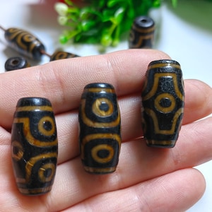 May include: Three brown and black agate beads with a geometric pattern. The beads are on a hand.