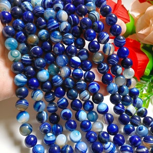 May include: Strands of round, polished beads in shades of blue and white. The beads have a marbled appearance, with swirling patterns. The beads are strung together, and appear to be made of a stone material.