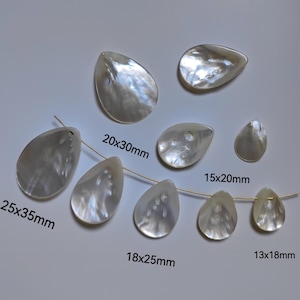 Może przedstawiać: Zestaw białych, perełkowatych zawieszek w kształcie łzy, w różnych rozmiarach. Zawieszki są nawleczone na złoty drut. Wymiary każdej zawieszki są podane pod każdą zawieszką. 25x35mm, 20x30mm, 18x25mm, 15x20mm, 13x18mm.