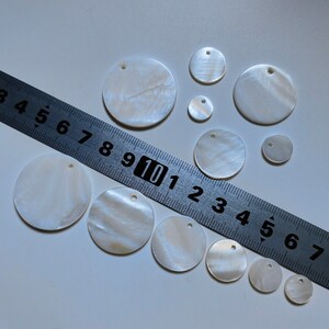 May include: Assortment of white mother of pearl shell circles with holes in the center. The circles range in size from approximately 1 inch to 2 inches in diameter.