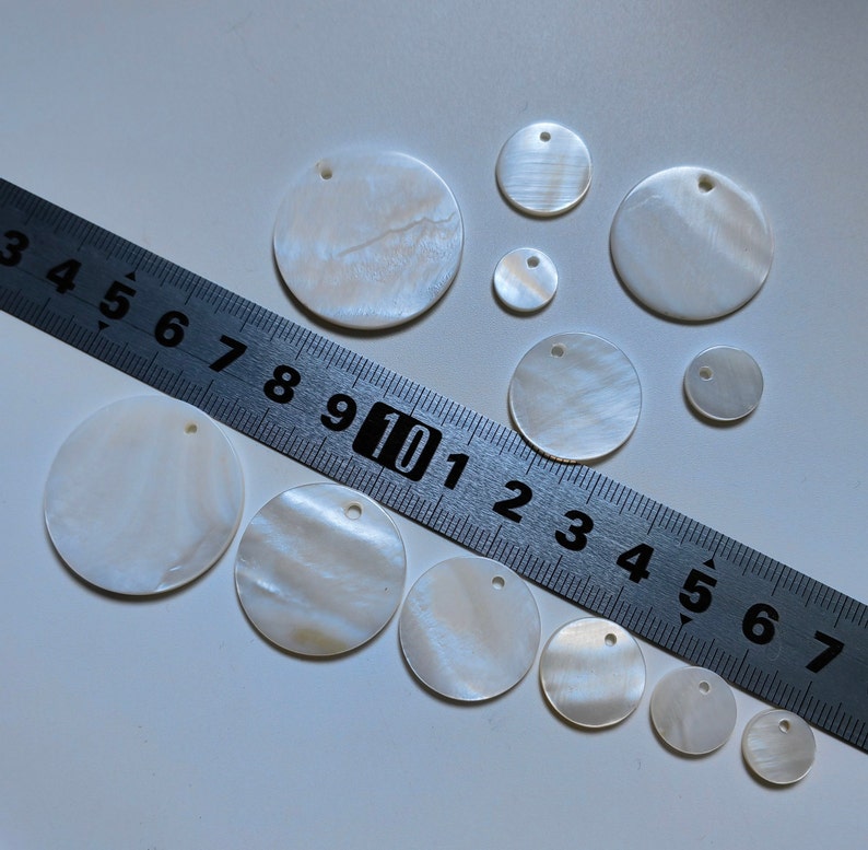 May include: Assortment of white mother of pearl shell circles with holes in the center. The circles range in size from approximately 1 inch to 2 inches in diameter.