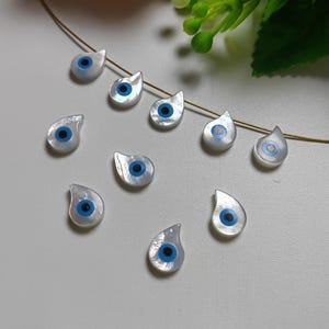 May include: Ten white teardrop-shaped beads with blue evil eye charms. The beads have a pearlescent finish.