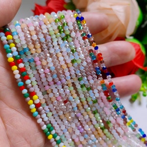May include: A collection of colorful glass beads, including clear, white, pink, green, blue, and red beads. The beads are strung on a string and are arranged in a row.