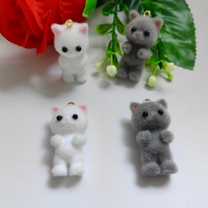 May include: Four fuzzy cat charms in white and gray. The charms are made of soft, plush fabric and have black eyes. They are perfect for adding a touch of whimsy to your jewelry or crafts.