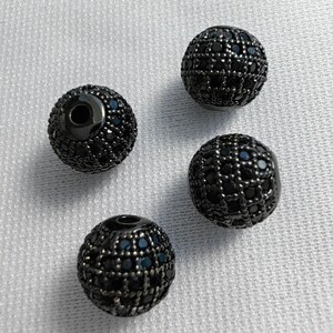 May include: Four black round beads with a black diamond-like pattern. The beads have a hole in the centre for stringing.