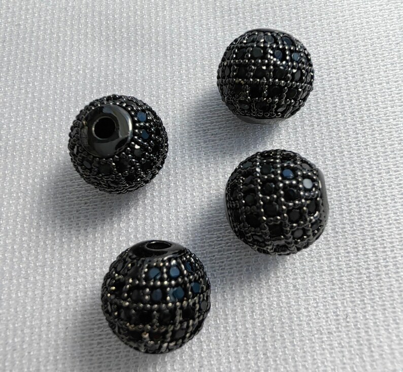 May include: Four black round beads with a black diamond-like pattern. The beads have a hole in the centre for stringing.