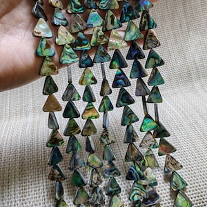 May include: A strand of iridescent abalone shell triangle beads. The beads are a mix of green, blue, and gold colours.