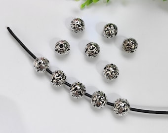 May include: Silver metal beads with a decorative floral pattern. The beads are strung on a black cord.