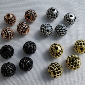 May include: Assortment of 14 black and silver beads with a faceted design. The beads are round and have a shiny finish.