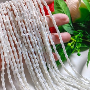 以下が含まれることがあります： 竹のような形をした白い貝殻のビーズの糸。ビーズはわずかに虹色に光る。