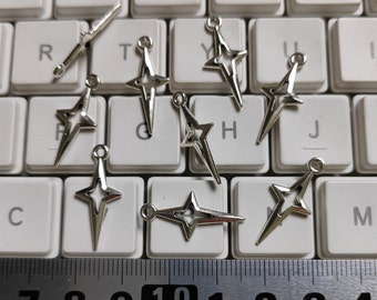 Puede incluir: Una colección de diez abalorios en forma de estrella plateados con un agujero en la parte superior para sujetarlos a joyas u otras manualidades. Los abalorios están dispuestos en un teclado y una regla.