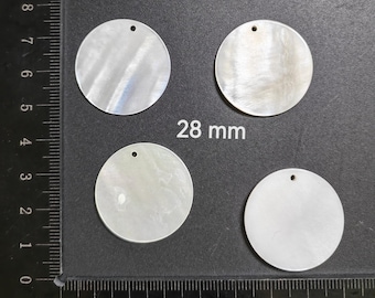 Puede incluir: Cuatro discos redondos de nácar blanco iridiscente con un agujero en el centro. Los discos tienen un diámetro de 28 mm y están dispuestos en semicírculo sobre una superficie negra.
