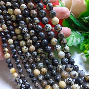 May include: A strand of round, black and white speckled beads. The beads are approximately 6mm in diameter and have a natural, earthy look.