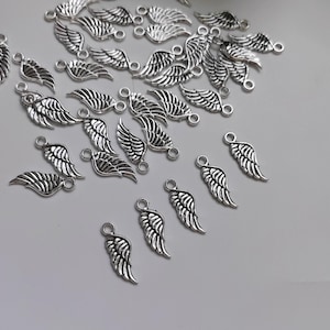 May include: A large quantity of silver-toned metal angel wing charms. The charms are small and delicate, with a loop at the top for attaching to jewellery or other crafts.