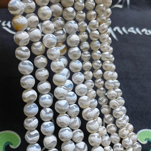 May include: A strand of white agate beads with gray and white stripes. The beads are round and have a smooth, polished finish.