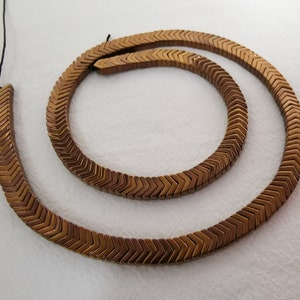 May include: A strand of brown chevron-shaped hematite beads with a black cord.