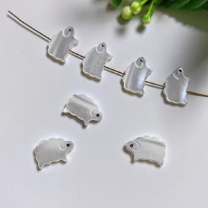 May include: A set of six white mother of pearl sheep charms with black eyes. The charms are strung on a gold wire.
