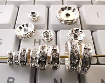 May include: A close-up of a set of silver-toned bead caps with clear rhinestones. The bead caps are arranged in a row on a white keyboard.