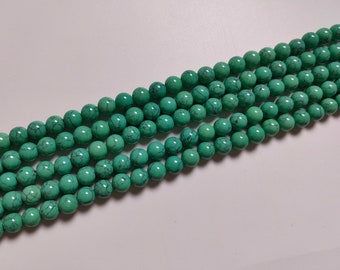 May include: A strand of turquoise green beads with a smooth, round shape. The beads have a mottled pattern and are strung together on a clear thread.