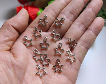 Puede incluir: Una colección de dijes en forma de estrella de metal plateado con un bucle en la parte superior. Los dijes están dispuestos en una mano.