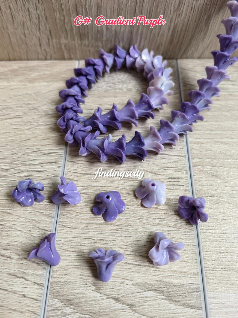 May include: A string of gradient purple flower-shaped beads arranged in a circular pattern, accompanied by several loose individual flower beads. The text G# Gradient Purple and findingscity are visible. The beads feature a smooth, glossy finish.