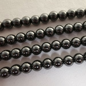 May include: A strand of black hematite beads. The beads are round and have a shiny, metallic finish.