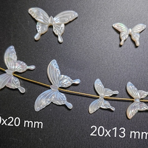 May include: Five iridescent white butterfly-shaped charms, two larger ones measuring 30x20 mm and three smaller ones measuring 20x13 mm. The charms are strung on a gold wire.