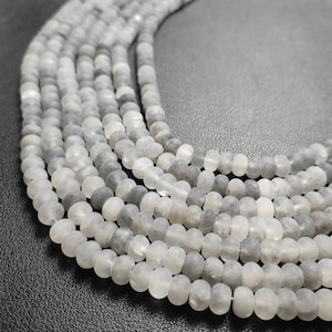 Könnte beinhalten: Eine Strähne aus weißen und grauen, mattierten Glasperlen. Die Perlen sind rund und haben eine glatte, matte Oberfläche.