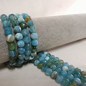 Può includere: Una collana di perle di agata blu con un motivo a marmi bianco e giallo. Le perle sono rotonde e hanno una finitura liscia e lucida.