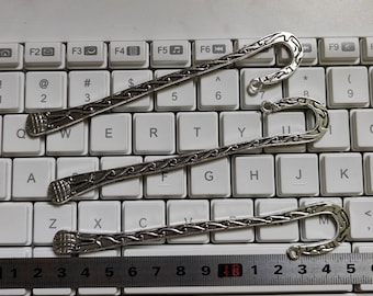 May include: Three silver bookmark holders with decorative designs. The bookmarks are laid out on a white keyboard with a ruler underneath.