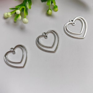 Può includere: Tre ciondoli argentati a forma di cuore a doppio strato con un anello in cima per appendere.
