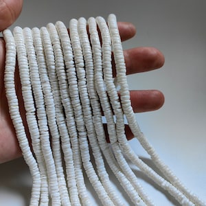 Op de afbeelding: Een streng witte schelp kralen, gemaakt van natuurlijke materialen. De kralen zijn klein en rond, en ze zijn aan elkaar geregen op een dun koord. De kralen zijn netjes en ordelijk gerangschikt, en ze zijn allemaal even groot en even gevormd.