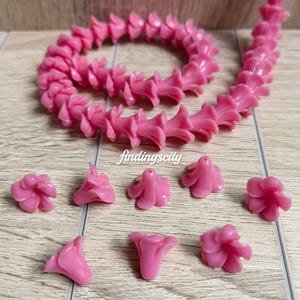 May include: A long strand of fuchsia-colored flower-shaped beads arranged in a coil, accompanied by several loose individual flower beads. The text D# Fuchsia and findingscity are visible. Each bead features a central hole for stringing.