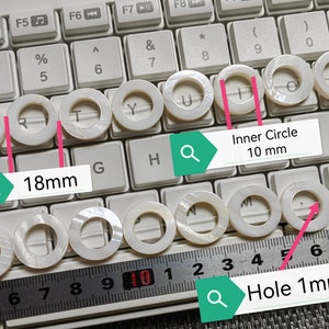 Könnte beinhalten: Weiße Perlmutt-Ringe mit einem Innendurchmesser von 10 mm und einem Loch von 1 mm. Die Ringe liegen auf einer Tastatur und einem Lineal, wobei die Maße beschriftet sind.