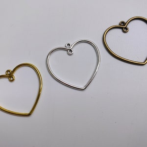 May include: Three heart-shaped metal frames for jewelry making. The frames are gold, silver, and bronze.