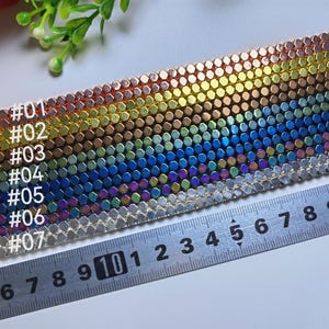 Può includere: Primo piano di una catena di metallo arcobaleno iridescente con sette colori diversi. La catena viene misurata con un righello, mostrando i numeri da 4 a 20.