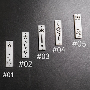 May include: Five rectangular, off-white pendants with decorative cut-out designs. Each pendant has a different pattern, including floral and abstract shapes. The pendants are numbered from #01 to #05 and are displayed against a dark background.