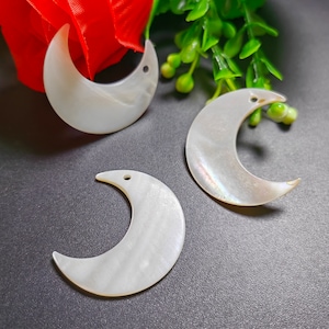 May include: Three white crescent moon shaped shell charms with a hole at the top for hanging.