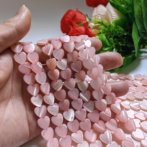 Op de afbeelding: Een streng roze hartvormige kralen gemaakt van parelmoer. De kralen zijn geregen op een doorzichtig elastiekkoord en zijn perfect voor het maken van sieraden.