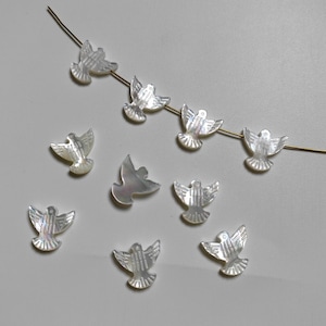 May include: A collection of white mother of pearl dove charms, some strung on a gold wire. The doves have a detailed design and are perfect for jewellery making.