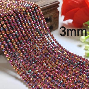Puede incluir: Una hebra de cuentas facetadas iridiscentes en tonos rojos, dorados y verdes. Las cuentas tienen 3 mm de diámetro y están enhebradas en un hilo transparente. Las cuentas están dispuestas en un patrón suelto y fluido.